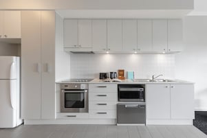 Uma cozinha moderna com arm ários brancos, forno embutido, lava-louças e pia de aço inoxidável.