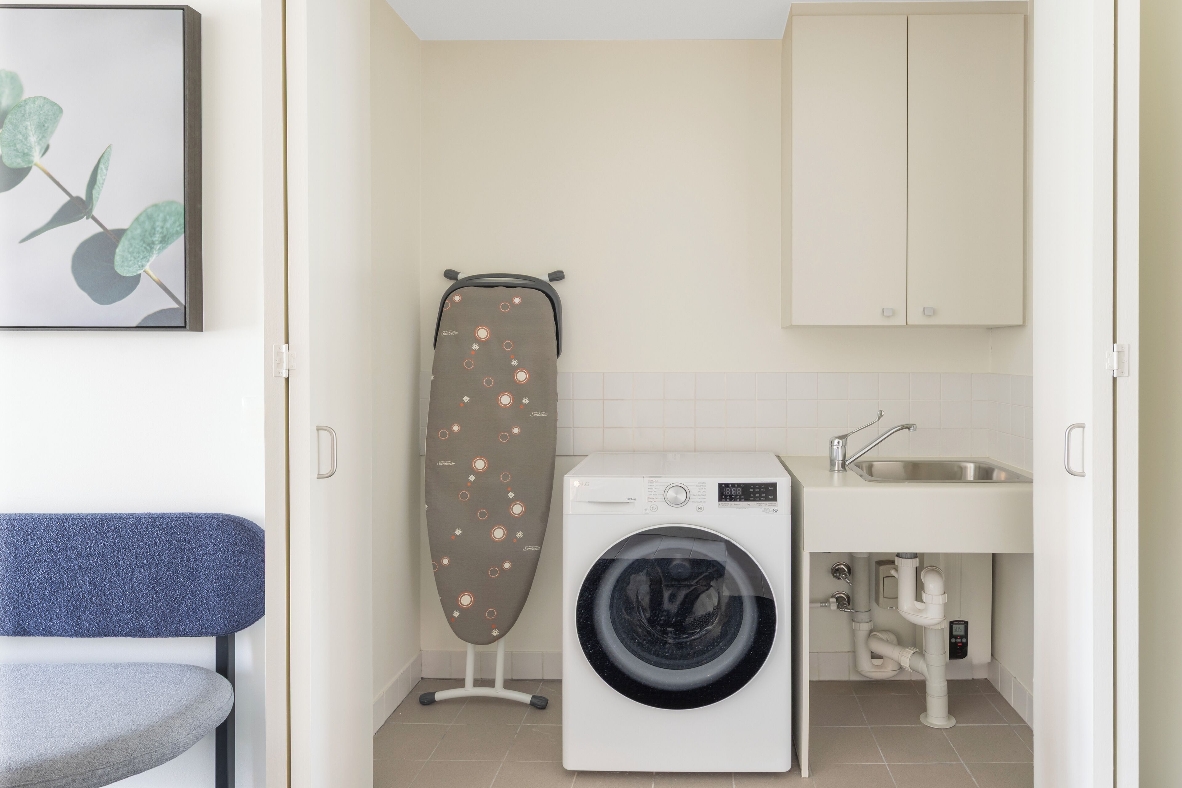 A compact laundry area with a washing machine, an ironing board, and a sink.