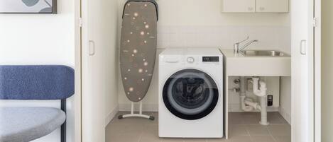 A compact laundry area with a washing machine, an ironing board, and a sink.