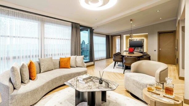 A modern living room with a curved sofa, a marble coffee table, and a dining area with a round table and chairs. - AHC Taksim Hotel (Istanbul)