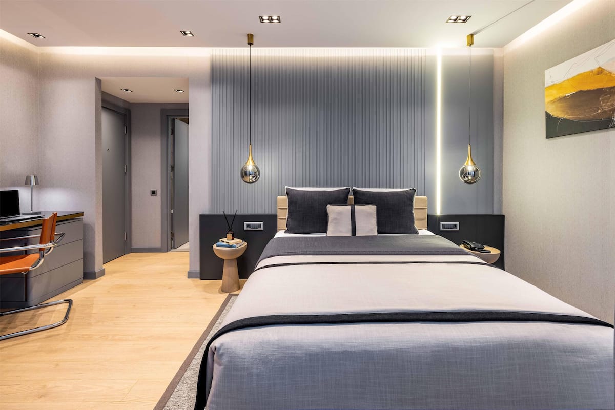 Quarto de hotel moderno com uma cama grande, mesas de cabeceira, uma escrivaninha e uma cadeira.
