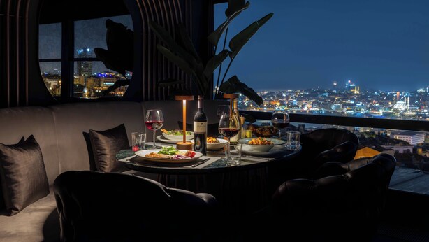 A dining area with a table set for two, a bottle of wine, and a view of a cityscape at night. - AHC Taksim Hotel (Istanbul)