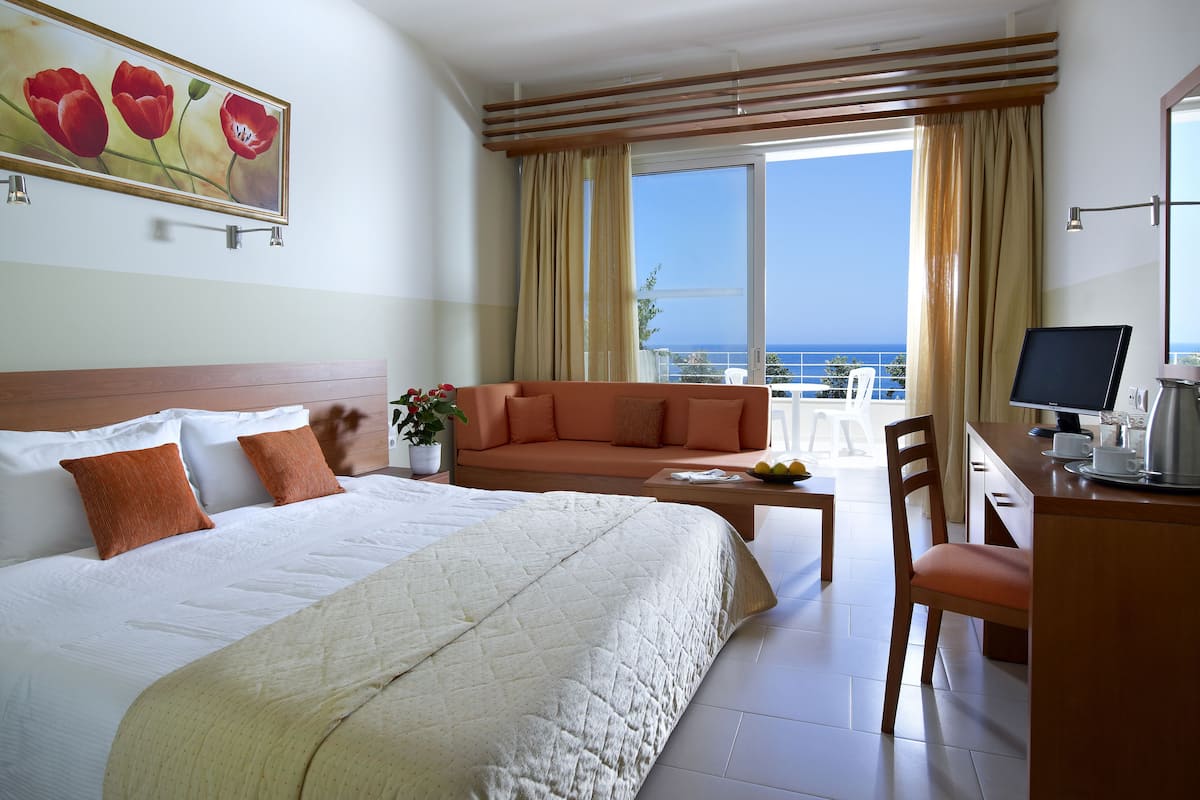A hotel room with a bed, a sofa, a desk with a computer, and a balcony with a view.