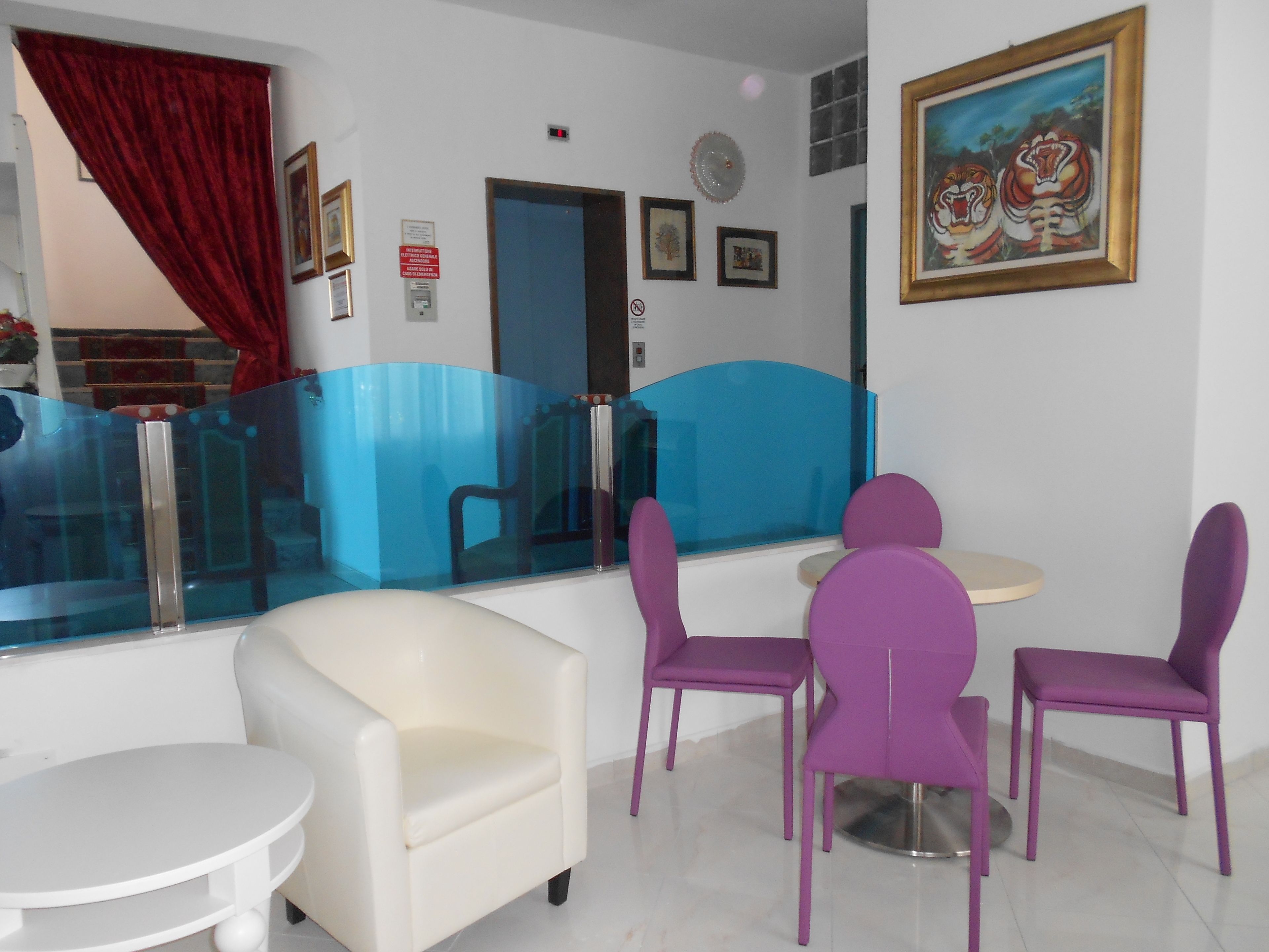 A dining area with purple chairs and a white table, a red curtain, and a painting of tigers on the wall.