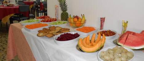 Uma mesa de buffet com diversos alimentos, incluindo frutas, legumes e petiscos.