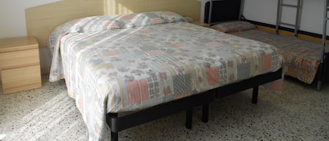 A bedroom with a single bed, a bunk bed, a wooden nightstand, a framed picture on the wall, and a tiled floor.