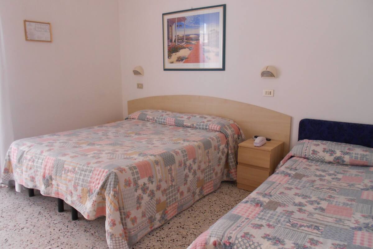 A bedroom with two beds, a wooden headboard, a nightstand, a framed picture on the wall, and a small bedside table with a lamp.