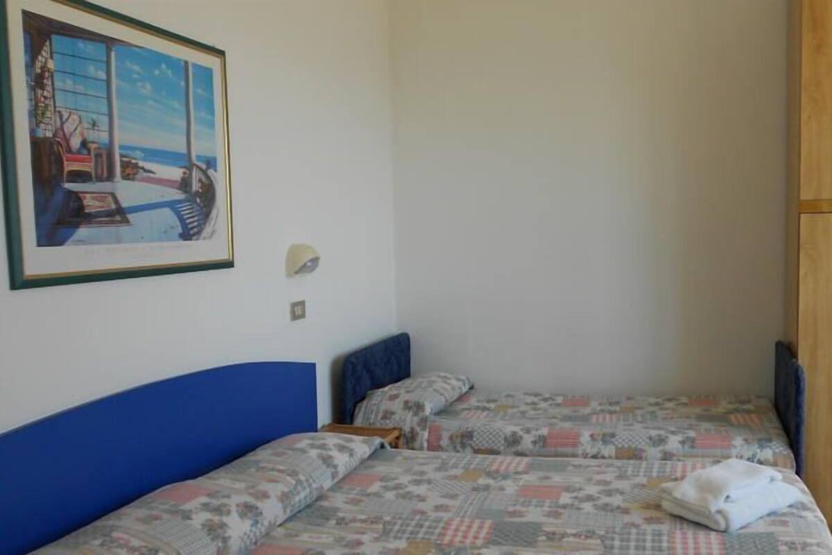 A bedroom with two beds, a wooden wardrobe, a framed picture on the wall, and a small bedside table.