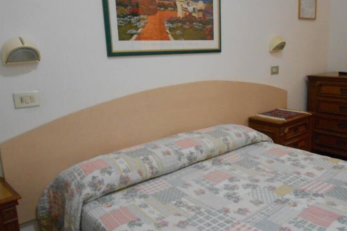A bedroom with a bed, a dresser, a nightstand, a framed picture on the wall, and a light switch.