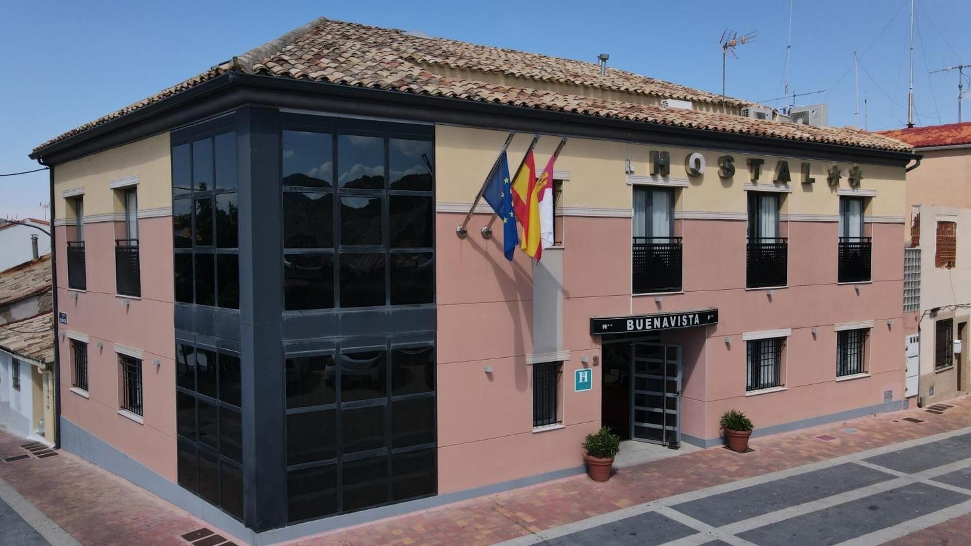 Un hotel con fachada de vidrio moderna, un cartel que dice 'BUENAVISTA' y varias banderas, incluida la bandera de la Unión Europea.
