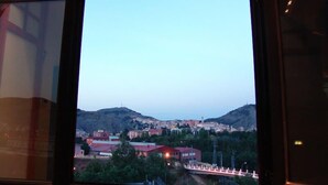 A view through a window of a town with buildings, a bridge, and hills in the background. - Hostal Buenavista (Cuenca)
