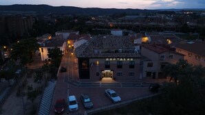 A building with a sign reading "HOSTAL" at dusk, surrounded by parked cars and a checkered pavement. - Hostal Buenavista (Cuenca)