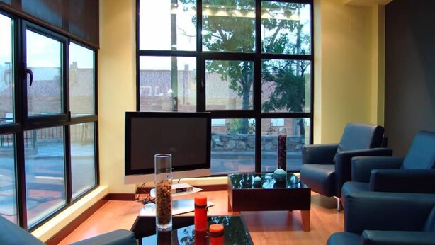 A modern living room with a large TV, comfortable seating, and a view through large windows. - Hostal Buenavista (Cuenca)