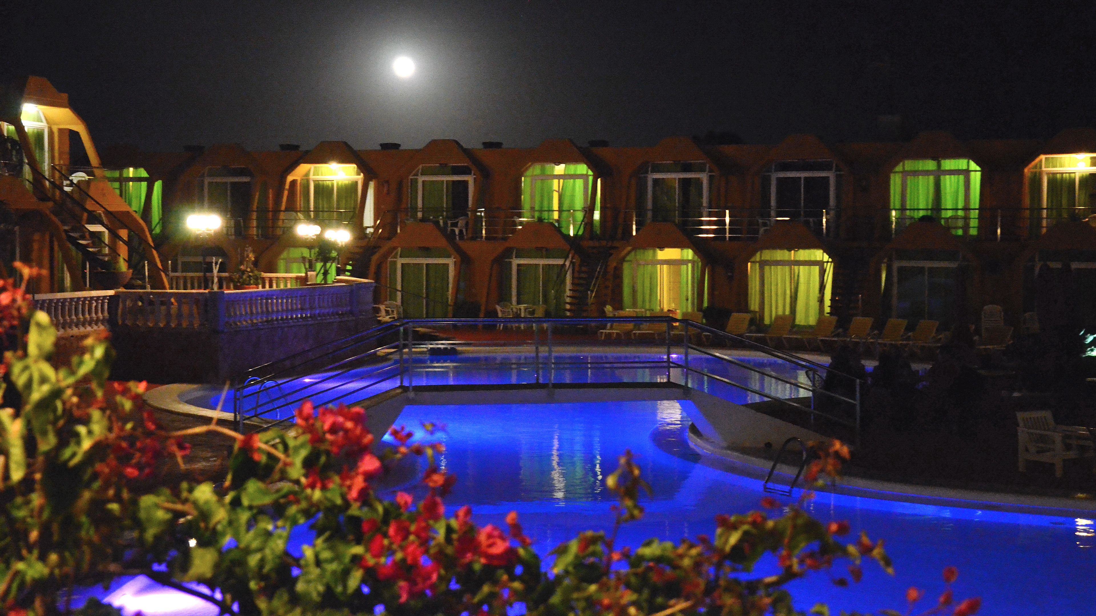 Ein Poolbereich mit Mond am Himmel, umgeben von Gebäuden mit grünen Vorhängen.