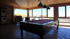 Una mesa de billar en una sala con ventanas amplias, un dardo y una máquina de billares.