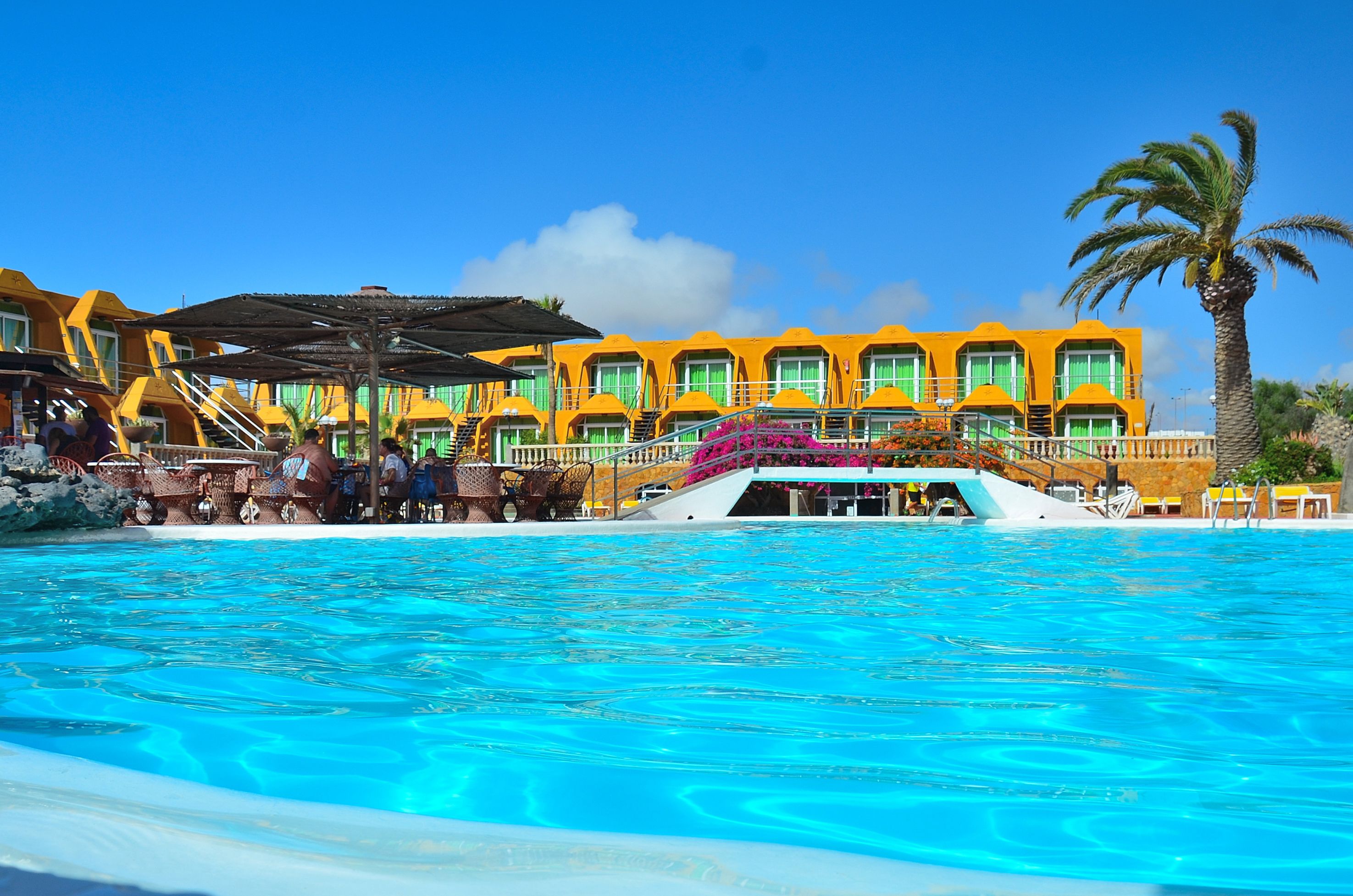 Un hôtel avec une piscine, des bâtiments jaunes et un palmier.