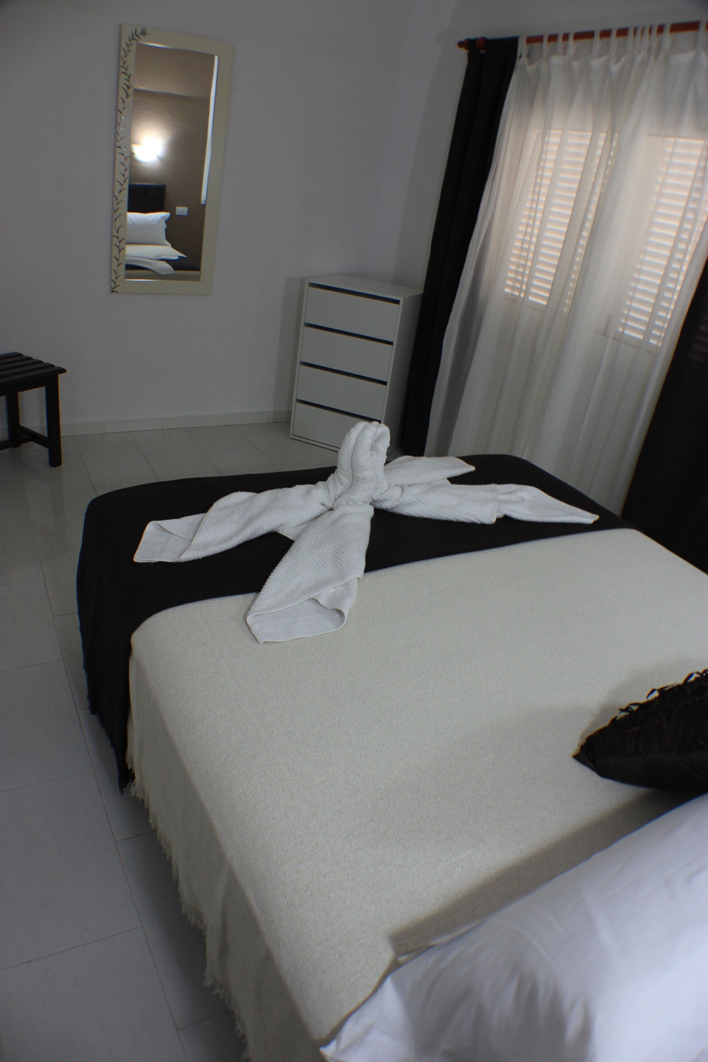 Habitación de hotel con cama, cómoda, espejo y ventana con cortinas.