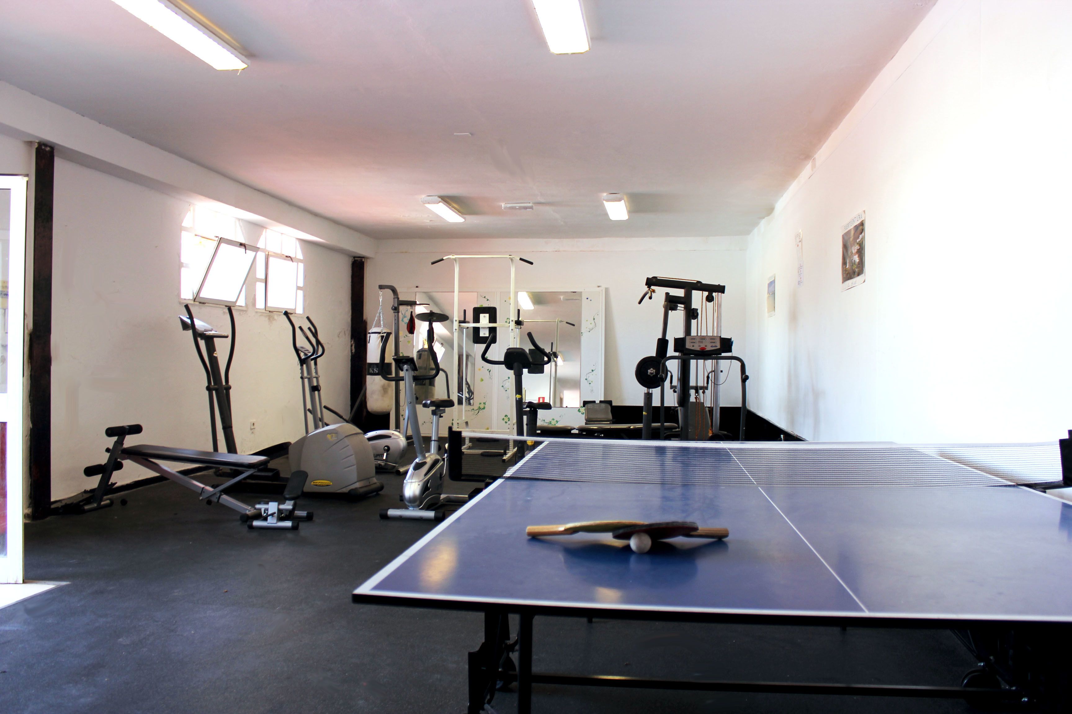Une salle de sport équipée de matériel d’exercice, d’une table de ping-pong et d’une fenêtre laissant entrer la lumière naturelle.