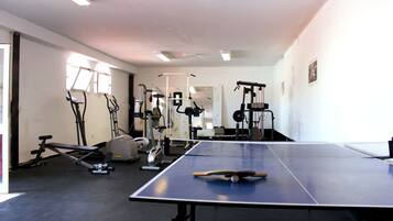 Une salle de sport équipée de matériel d’exercice, d’une table de ping-pong et d’une fenêtre laissant entrer la lumière naturelle.