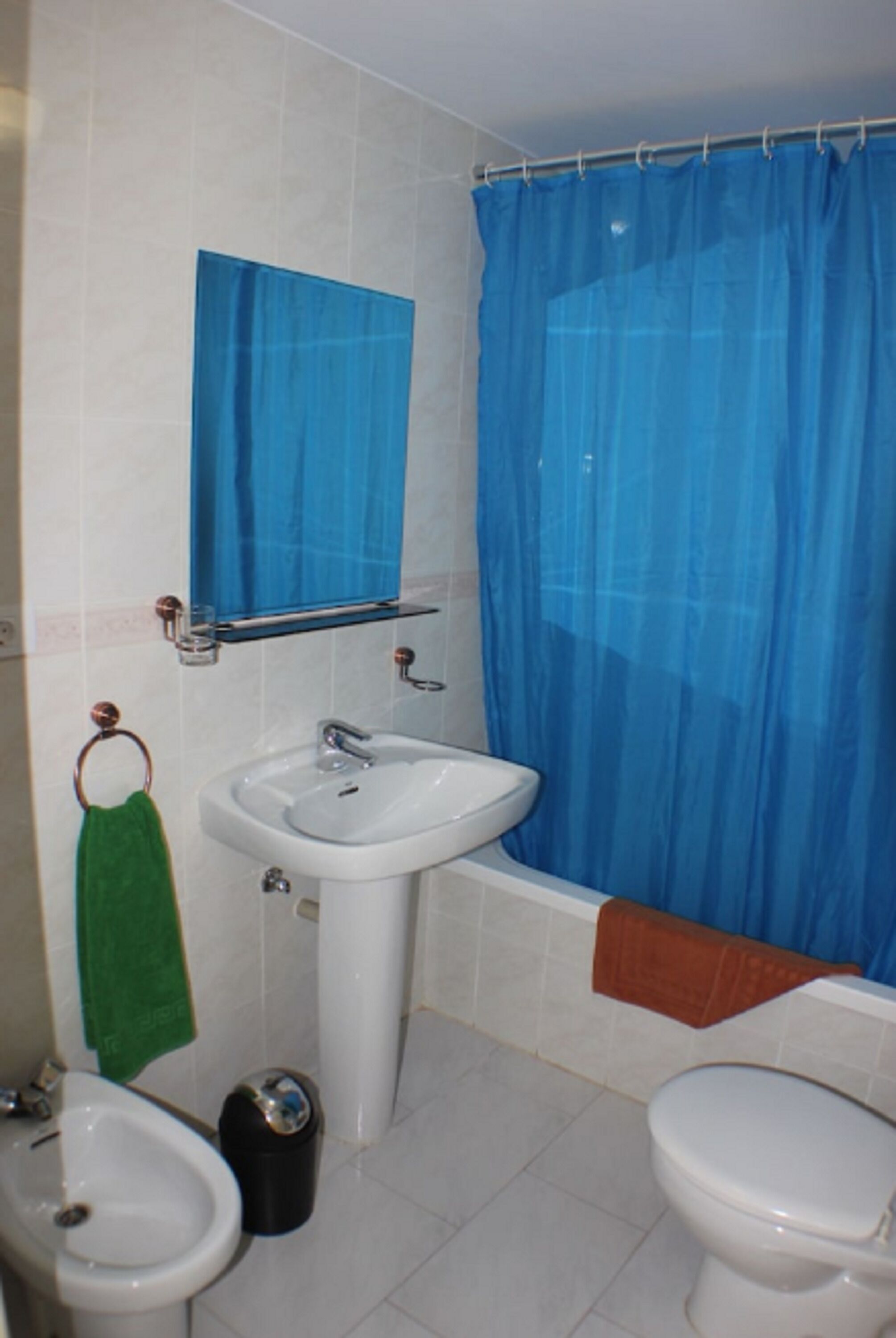Un baño con un lavamanos blanco, un espejo, una cortina de ducha azul, una toalla verde y un inodoro blanco.