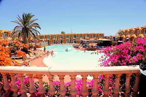 Zona de piscina de hotel con piscina azul cristalina, tumbonas y una palmera.