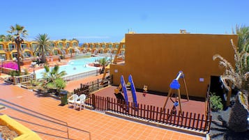Ein Resort mit Schwimmbad, Palmen und einem eingezäunten Spielbereich.