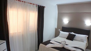 Una habitación de hotel con cama, cortinas blancas y cabecero con luces.