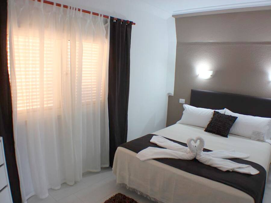 A hotel room with a bed, white curtains, and a headboard with lights.