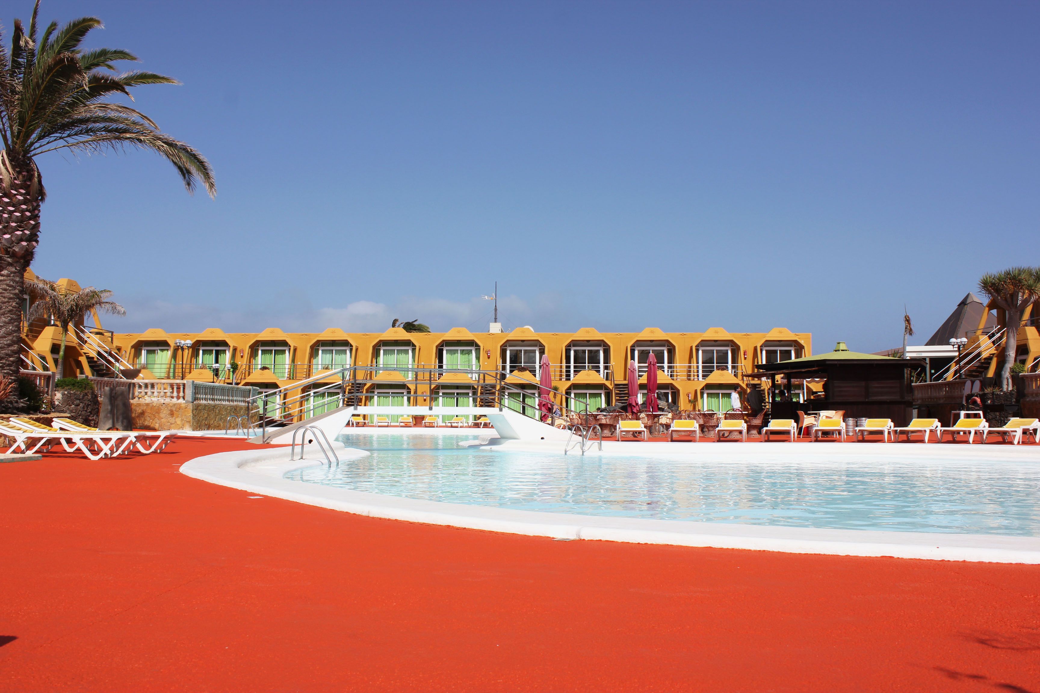 A hotel with a pool, sun loungers, and palm trees.