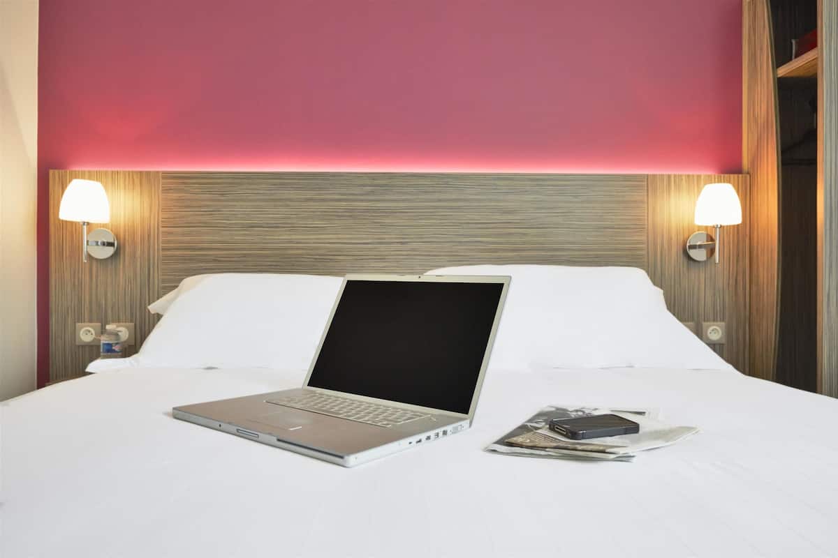 A hotel room with a bed, a laptop, and a magazine on the bed.