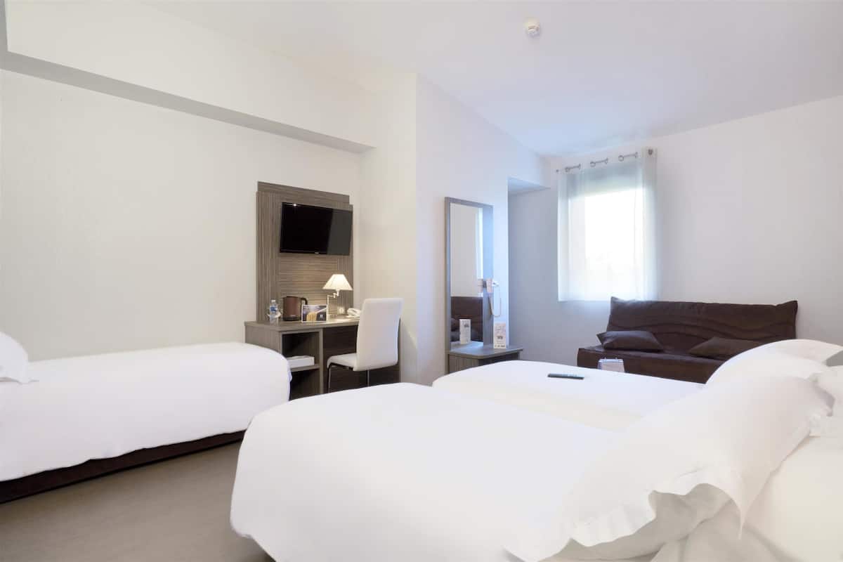 A hotel room with two single beds, a desk with a chair, a flat-screen TV, a mirror, and a window with curtains.