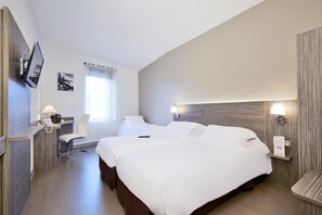 Habitación de hotel con una cama grande, un escritorio con lámpara, un televisor montado en la pared y una ventana con cortinas.
