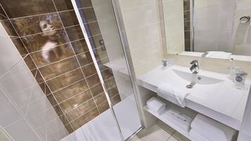 A modern bathroom with a glass shower enclosure, a white sink with a mirror, and neatly arranged towels.
