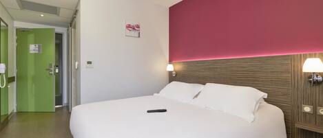Une chambre d’hôtel avec un grand lit, une porte verte, un mur d’accent rouge et une lampe fixée au mur.