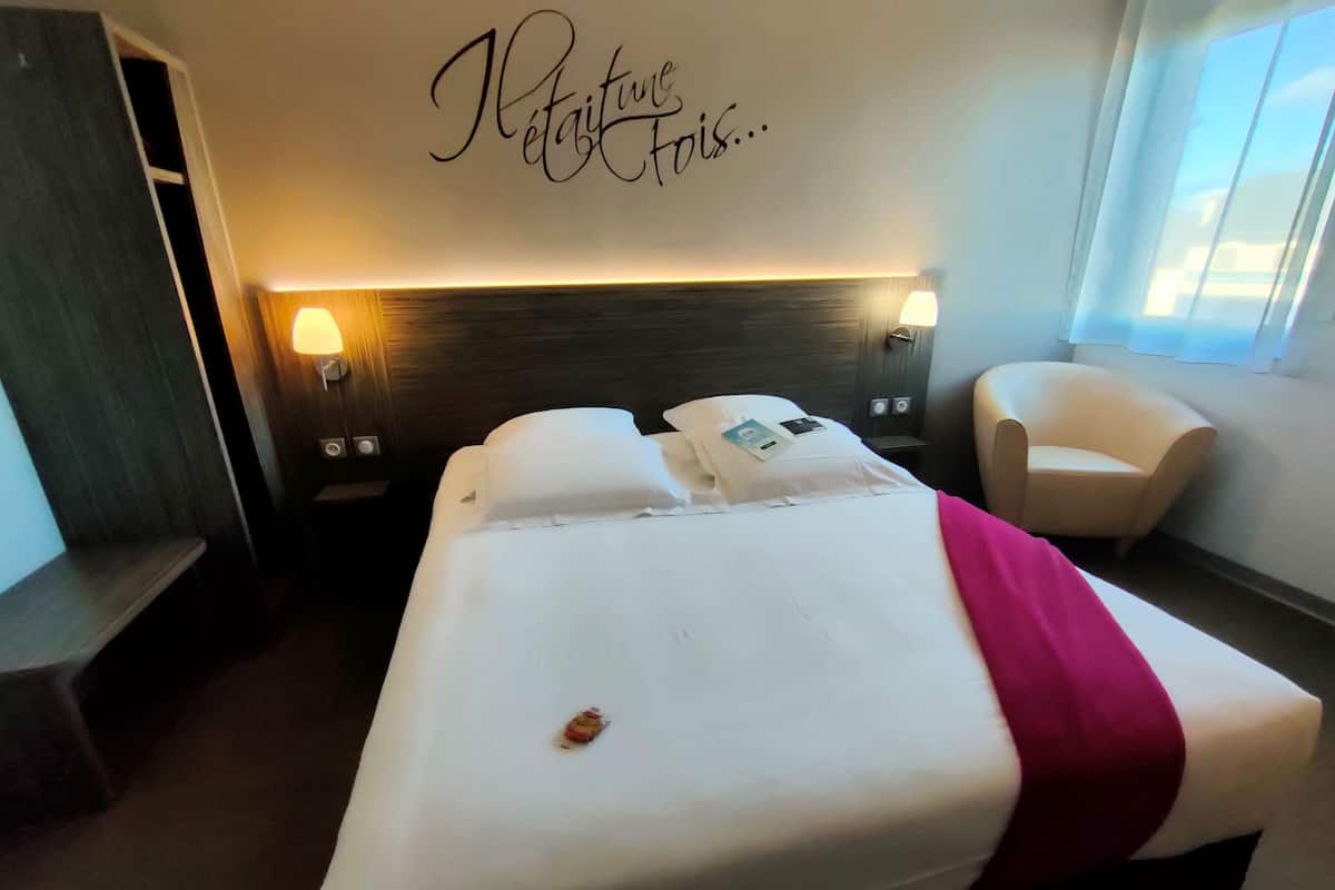 A hotel room with a large bed, two bedside lamps, a chair, and a wall with the text "Metamorphosis".