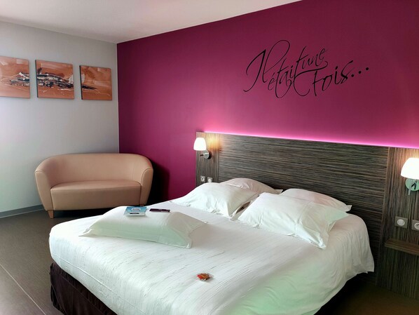 A hotel room with a bed, a chair, a wall with a sign, and a lamp. - Kyriad Saint Chely d'Apcher - Aire de la Lozère (Albaret-Sainte-Marie)