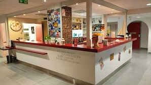A hotel reception area with a red counter, a world clock, and a wall decorated with travel posters. - Kyriad Saint Chely d'Apcher - Aire de la Lozère (Albaret-Sainte-Marie)