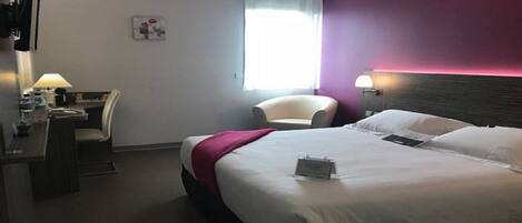 A hotel room with a bed, a desk, a chair, and a window.