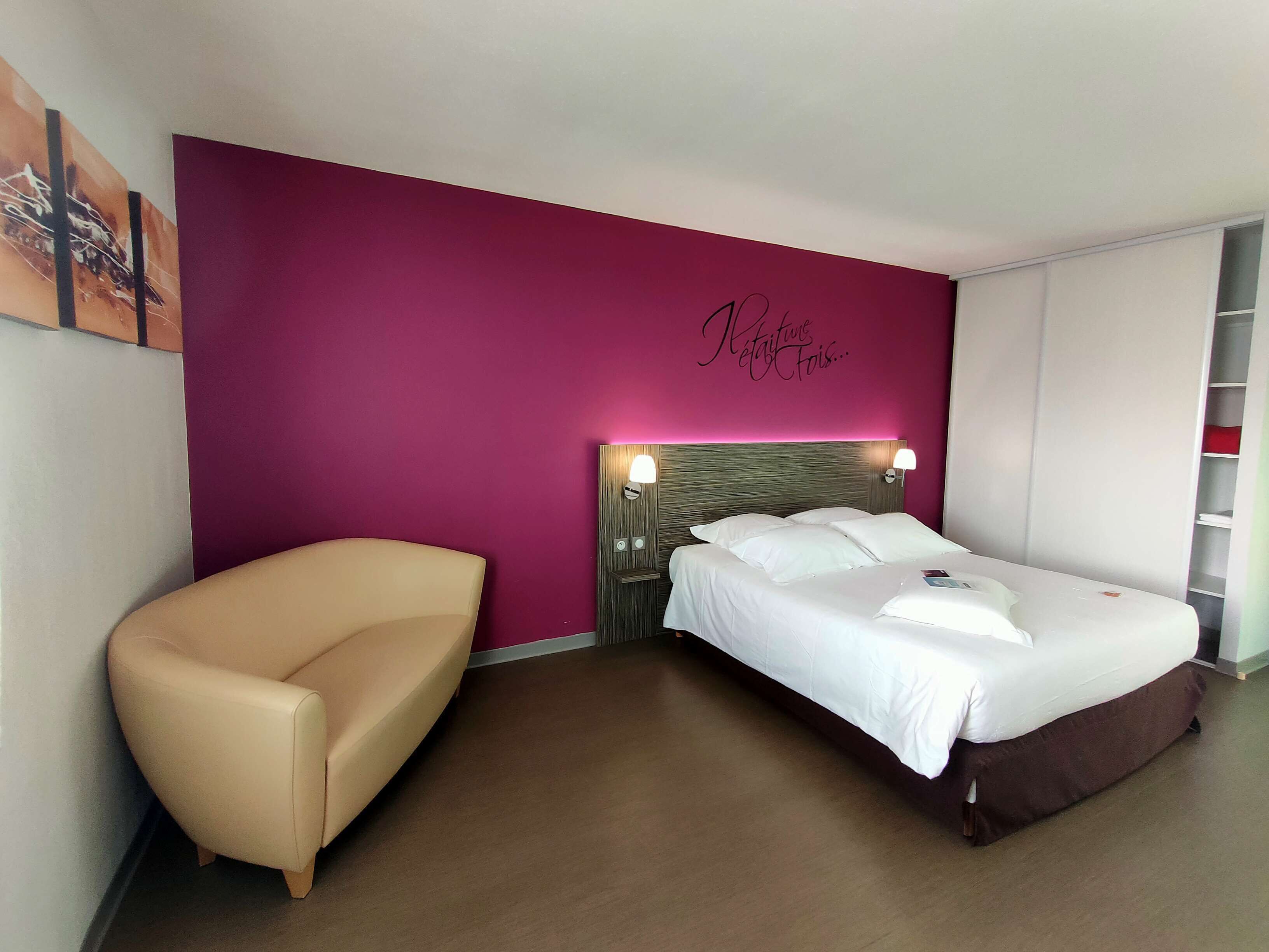 A hotel room with a bed, a chair, and a wall with a decorative sign.