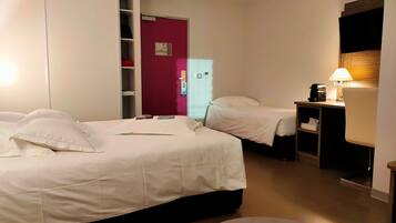 A hotel room with two beds, a desk with a lamp, a wardrobe, and a TV mounted on the wall.
