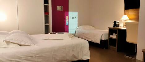A hotel room with two beds, a desk with a lamp, a wardrobe, and a TV mounted on the wall.