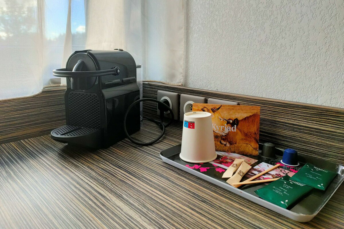 Una bandeja con una cafetera, una taza, una revista y artículos de aseo sobre una mesa a rayas cerca de una ventana.