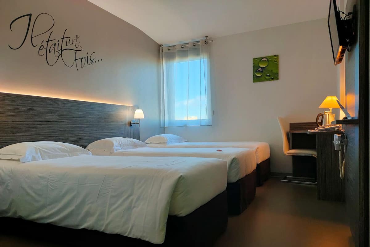 A hotel room with two beds, a desk with a lamp, a window with curtains, and a wall with a sign.