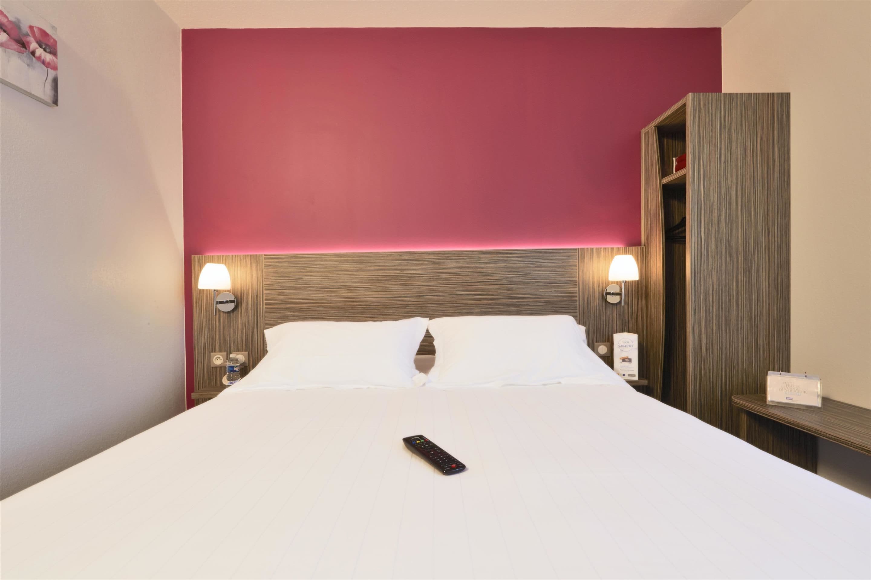 A hotel room with a large bed, a wooden headboard, two bedside lamps, and a nightstand with a lamp.