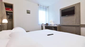 Ett hotellrum med en stor säng, ett skrivbord med en stol, en tv som är monterad på väggen och ett fönster med gardiner.