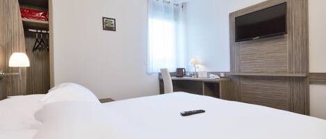 A hotel room with a large bed, a desk with a chair, a TV mounted on the wall, and a window with curtains.