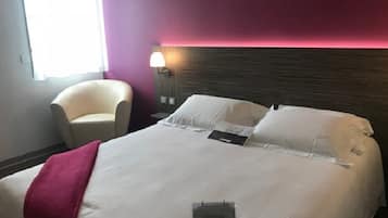 Ein Hotelzimmer mit einem Bett, einem Sessel, einem Nachttisch und einer Lampe.