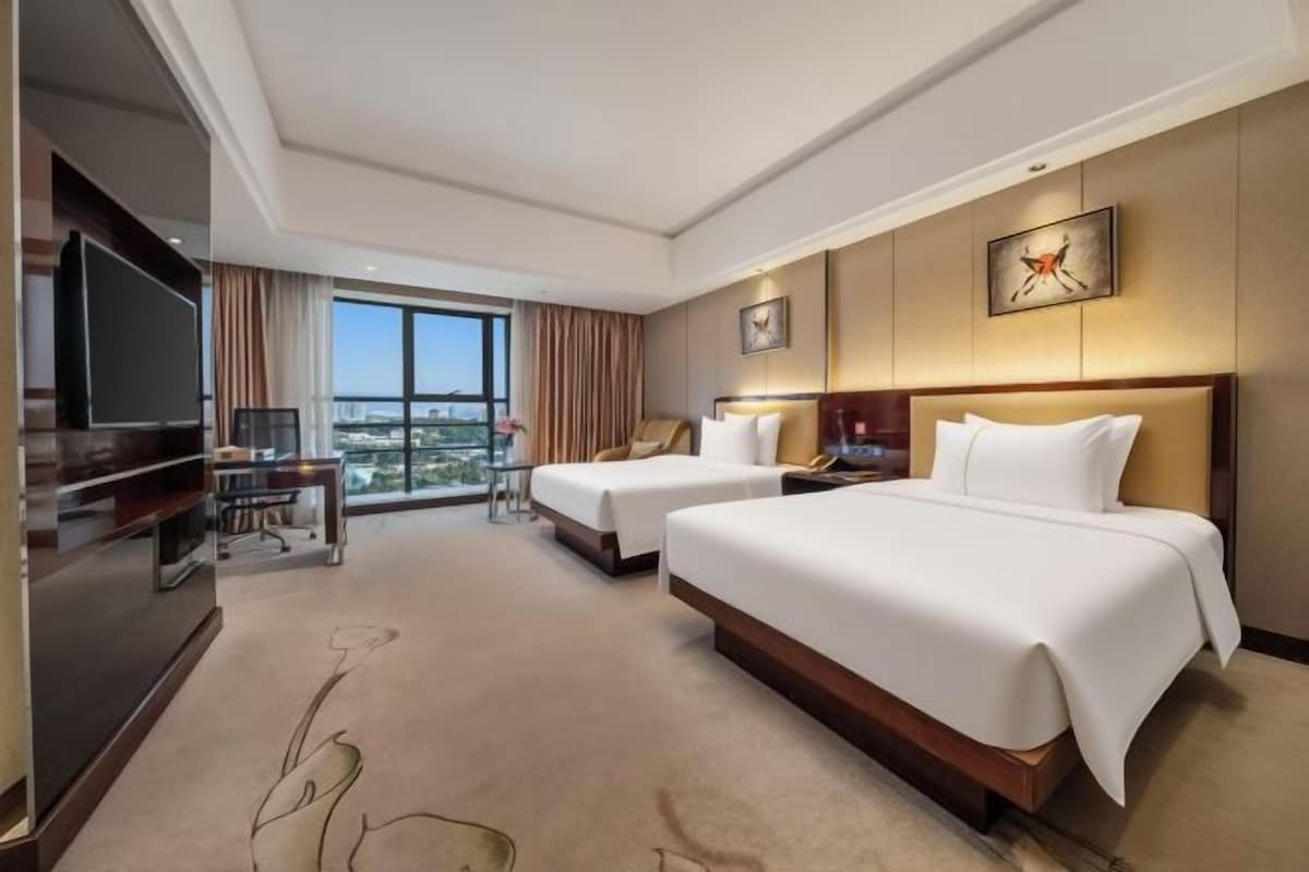Une chambre d’hôtel avec deux lits, une télévision, un bureau et une grande fenêtre donnant sur la ville.