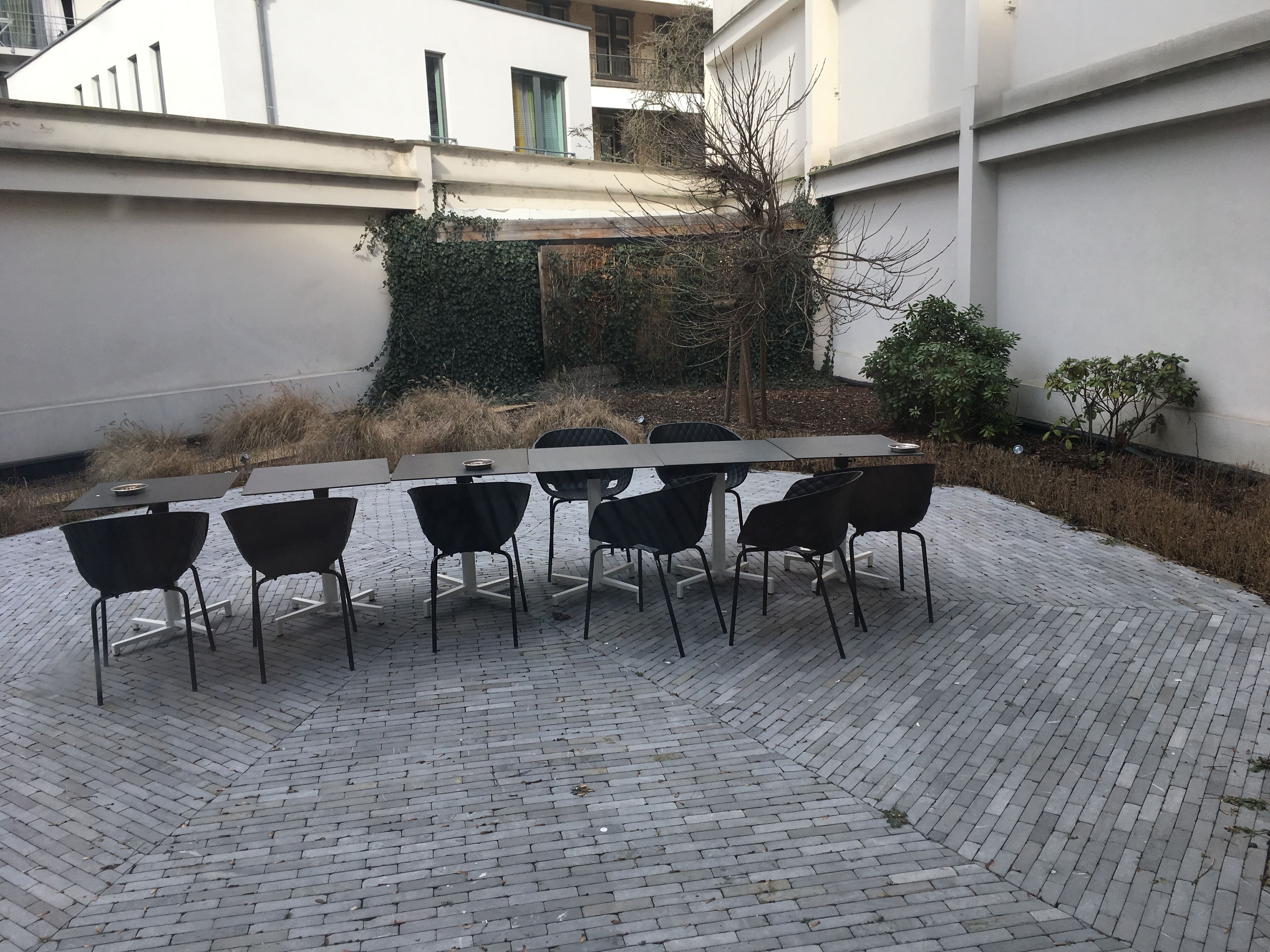Un patio con una mesa larga y seis sillas, rodeado de suelo de ladrillo y paredes blancas.