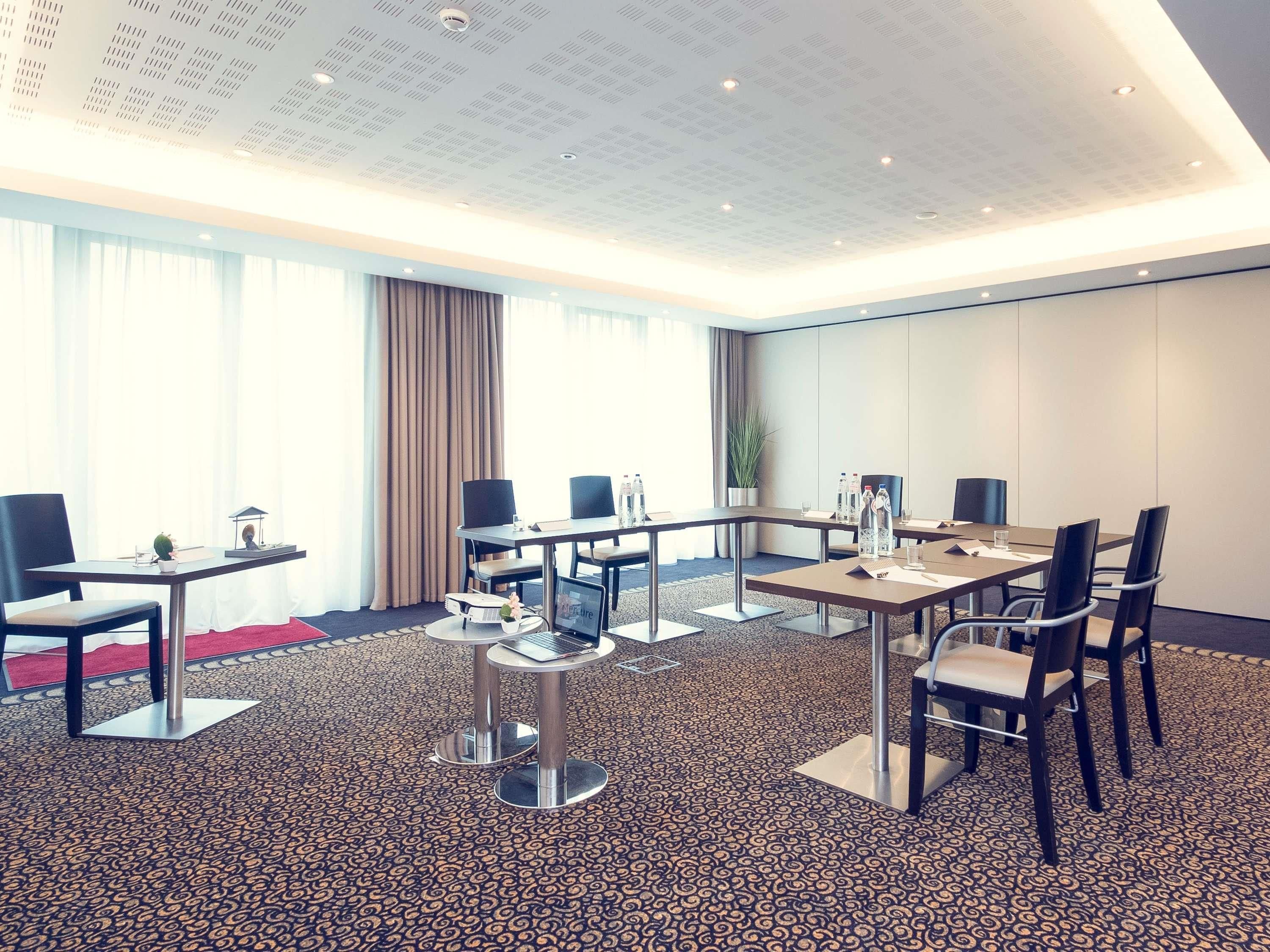 A conference room with a patterned carpet, multiple tables, chairs, and a large window with curtains.